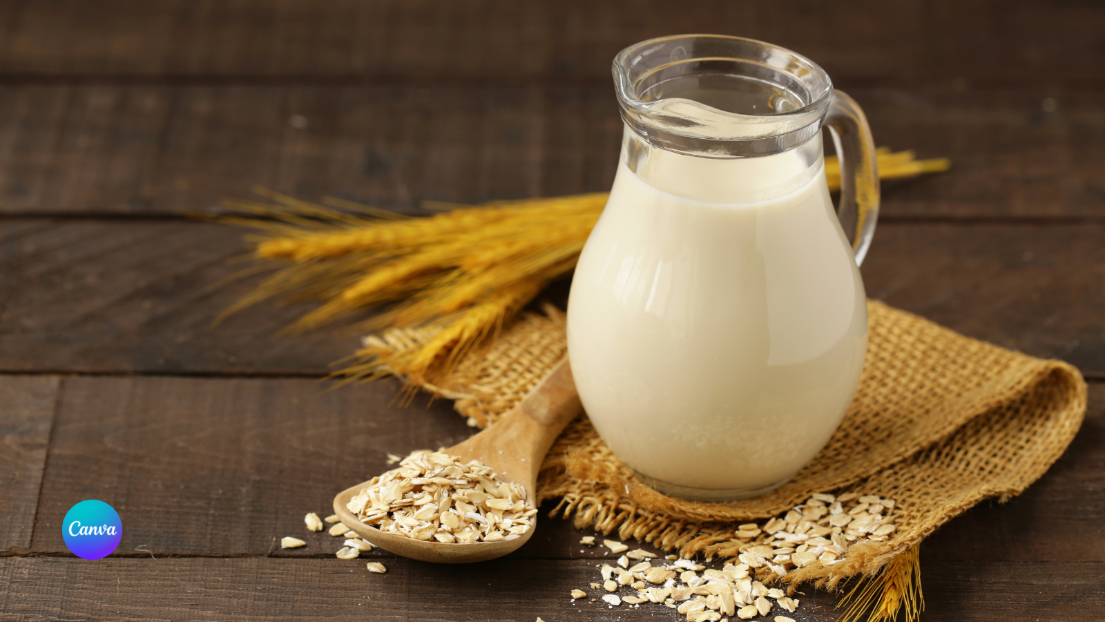 Zu sehen ist hier ein Glaskrug Hafermilch. Daneben sind Haferflocken verstreut.